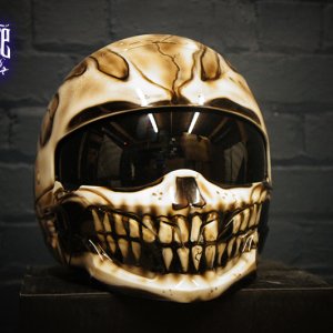 Gothic skull motorcycle helmet with cream and brown airbrush paint job featuring detailed jaw bones and teeth on black visor